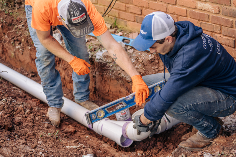 Two plumbers repairing water line outdoors with level
