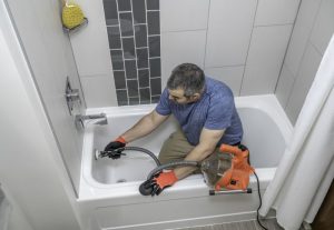 Plumber drain cleaning a bathtub with a plumbers snake