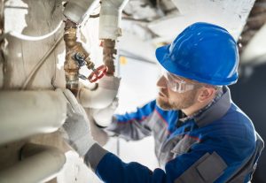 Male Worker Inspecting Water Valve For Leaks In Basement