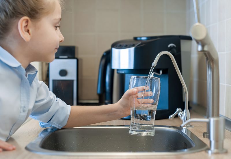 Child pouring fresh reverse osmosis purified water in kitchen at home.