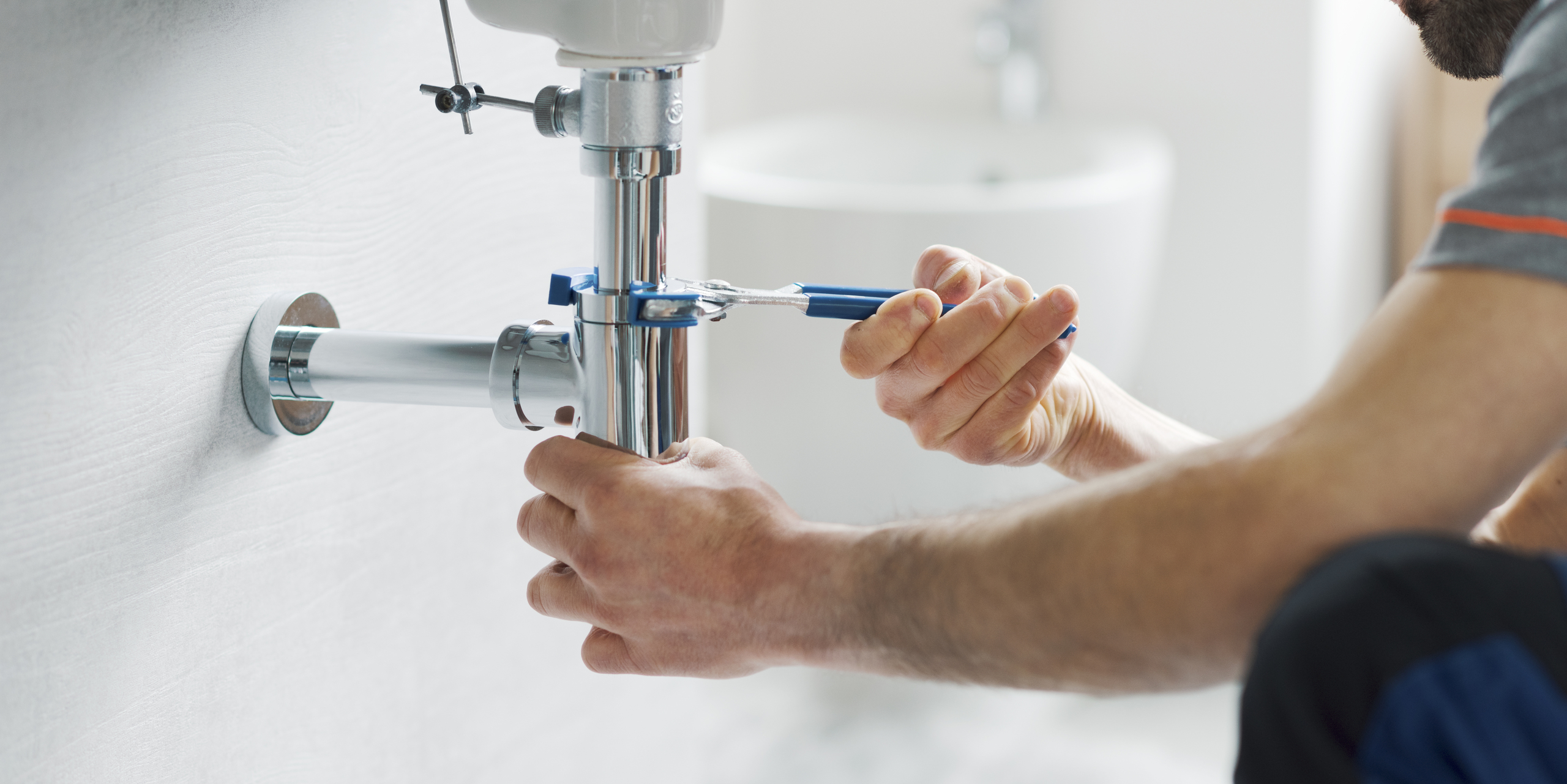 Plumber repairing a chrome sink drain with a wrench